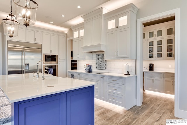 kitchen with stainless steel appliances, decorative light fixtures, white cabinets, light hardwood / wood-style floors, and an island with sink