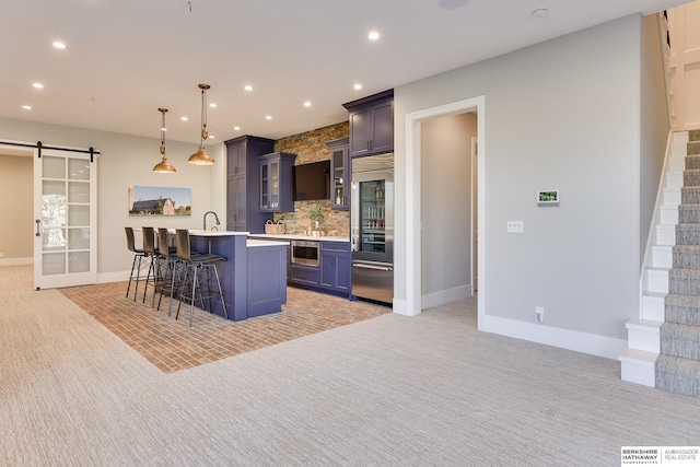 kitchen featuring a breakfast bar, pendant lighting, a barn door, a center island with sink, and built in appliances