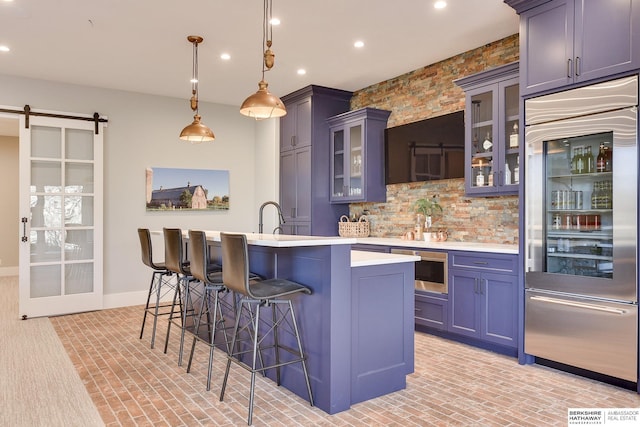 kitchen with tasteful backsplash, a kitchen breakfast bar, a barn door, built in appliances, and decorative light fixtures