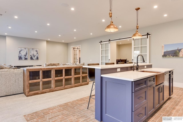 kitchen with sink, hanging light fixtures, a barn door, a kitchen bar, and a center island with sink