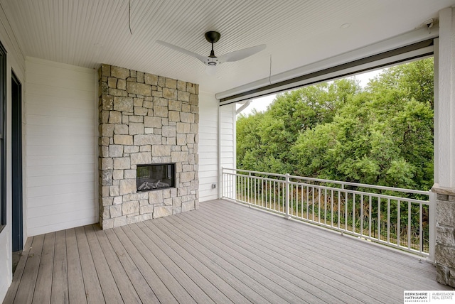 wooden deck with ceiling fan and an outdoor stone fireplace