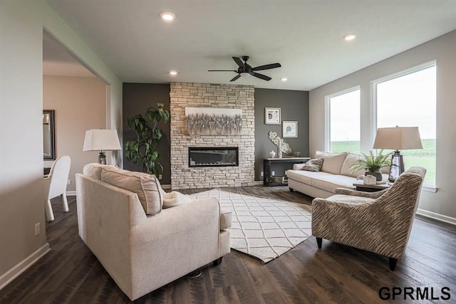 living room with ceiling fan, dark hardwood / wood-style flooring, a stone fireplace, and a wealth of natural light