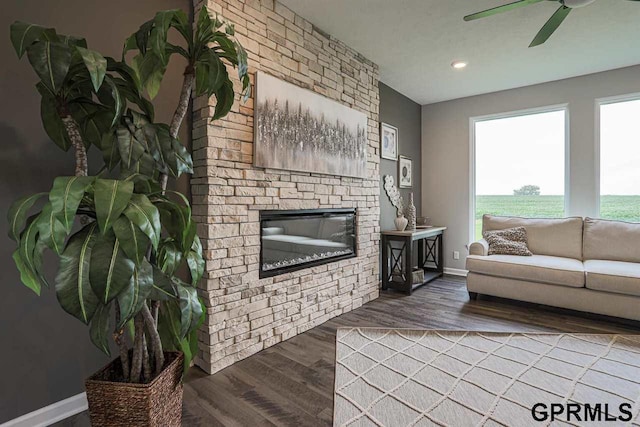 living room featuring a stone fireplace, ceiling fan, and dark hardwood / wood-style floors