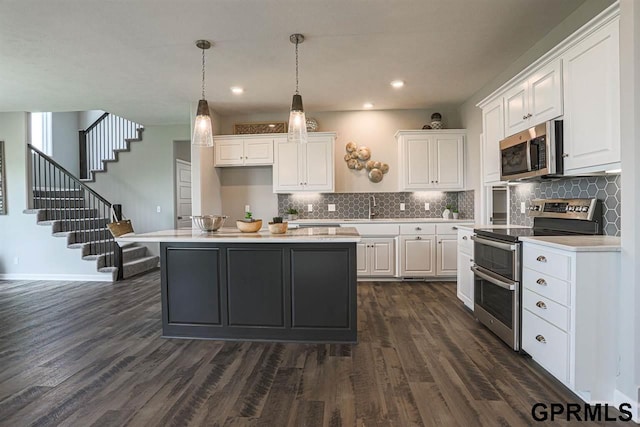 kitchen featuring appliances with stainless steel finishes, hanging light fixtures, white cabinets, and a kitchen island with sink