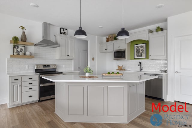 kitchen with a kitchen island, stainless steel appliances, wall chimney exhaust hood, and hanging light fixtures