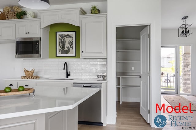 kitchen with dishwasher, hanging light fixtures, built in microwave, white cabinets, and sink