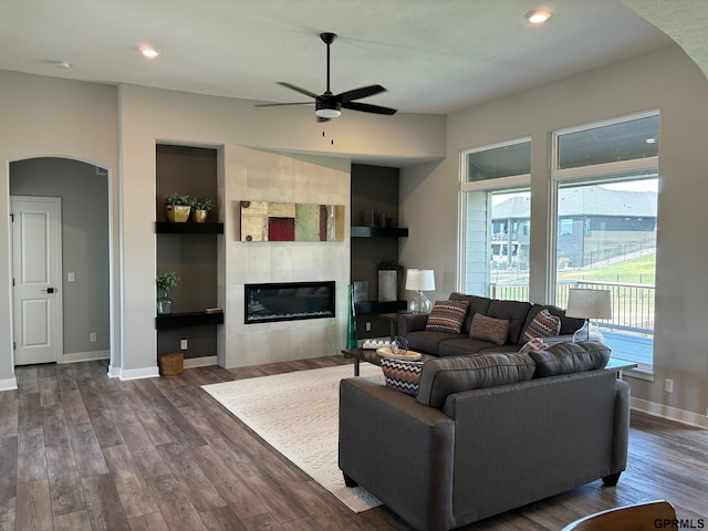 living area featuring baseboards, arched walkways, wood finished floors, and a tile fireplace