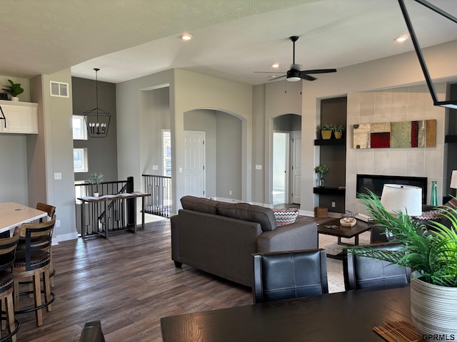 living room featuring arched walkways, dark wood finished floors, visible vents, a tile fireplace, and baseboards