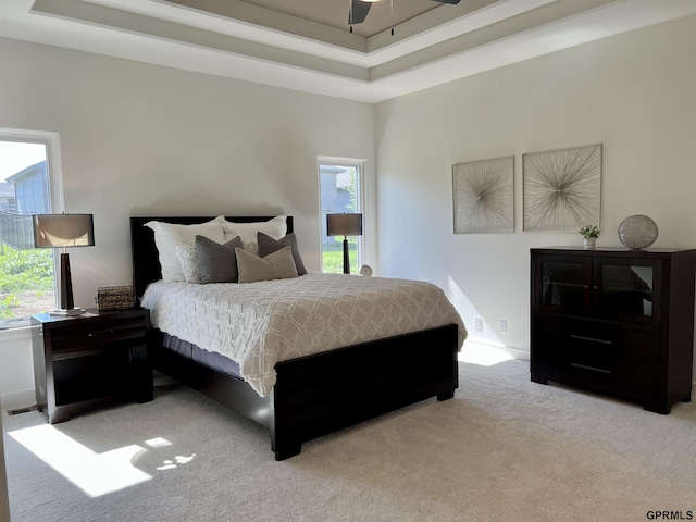 bedroom with light carpet, a tray ceiling, and a ceiling fan