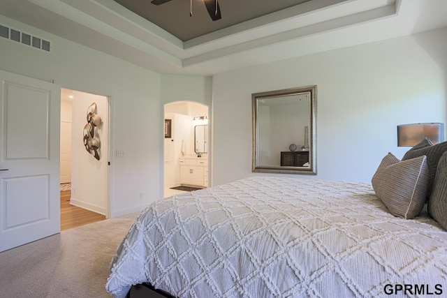 bedroom featuring visible vents, arched walkways, ensuite bathroom, a tray ceiling, and carpet floors