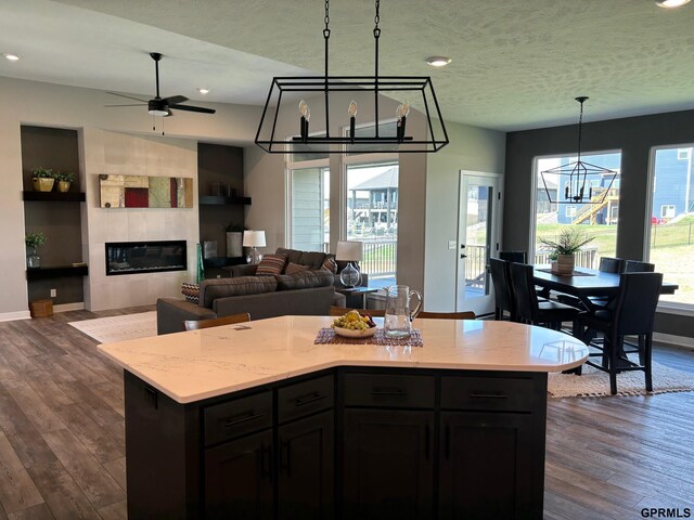 kitchen with a textured ceiling, a fireplace, baseboards, hanging light fixtures, and dark wood-style floors