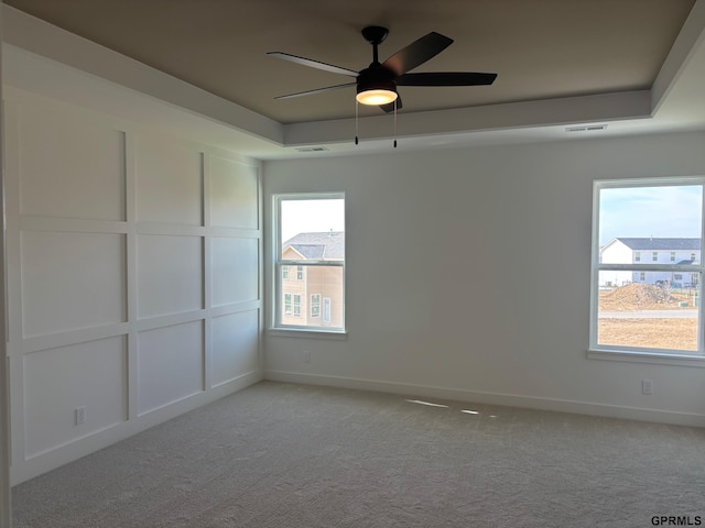 spare room featuring a raised ceiling, ceiling fan, and light colored carpet