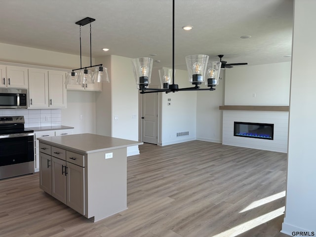 kitchen featuring a center island, white cabinets, hanging light fixtures, a fireplace, and appliances with stainless steel finishes