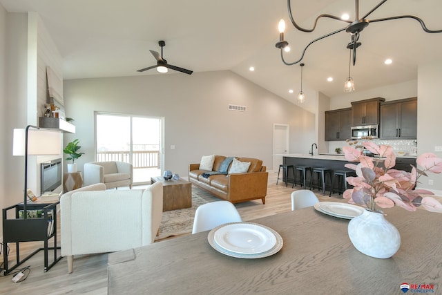 dining space featuring vaulted ceiling, ceiling fan with notable chandelier, and light wood-type flooring