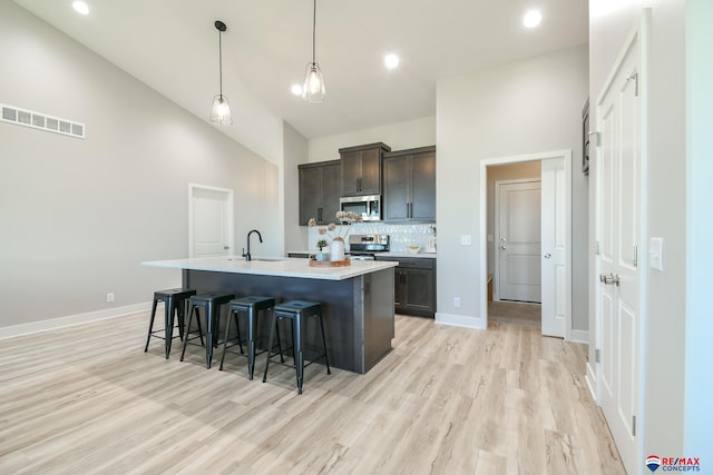 kitchen with appliances with stainless steel finishes, backsplash, dark brown cabinets, a kitchen island with sink, and decorative light fixtures