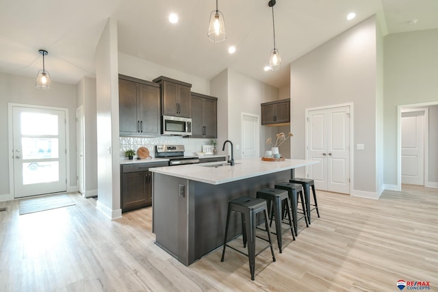 kitchen with appliances with stainless steel finishes, decorative light fixtures, high vaulted ceiling, and an island with sink