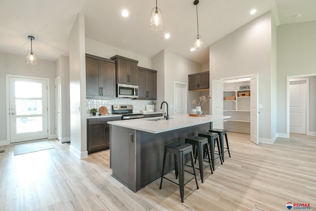 kitchen featuring hanging light fixtures, stainless steel appliances, high vaulted ceiling, and an island with sink