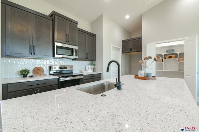 kitchen with sink, stainless steel appliances, light stone counters, backsplash, and dark brown cabinets