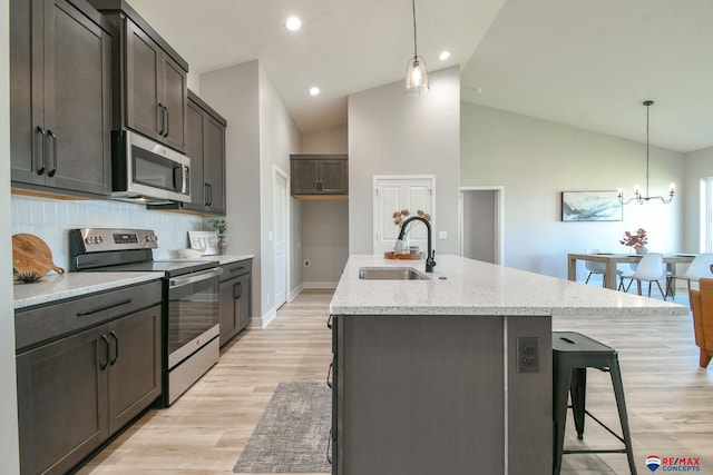 kitchen with sink, hanging light fixtures, stainless steel appliances, tasteful backsplash, and a kitchen island with sink