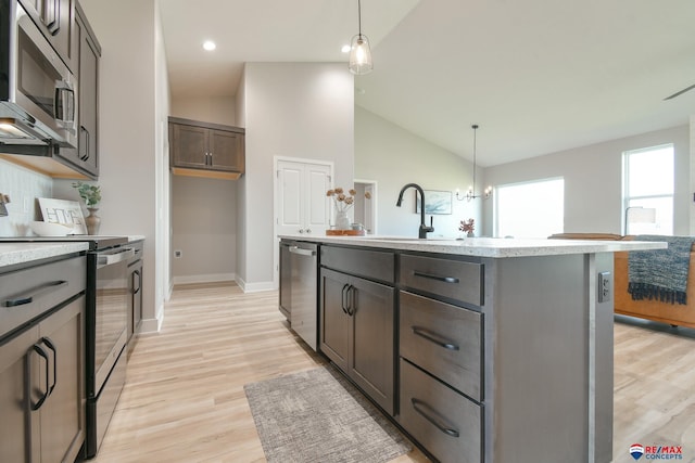 kitchen with hanging light fixtures, light hardwood / wood-style floors, lofted ceiling, a center island with sink, and appliances with stainless steel finishes