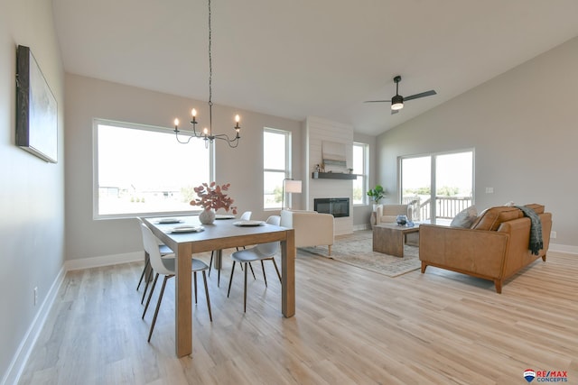 dining area with ceiling fan with notable chandelier, light hardwood / wood-style floors, lofted ceiling, and a fireplace