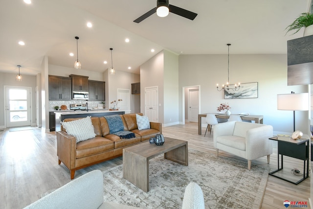 living room with high vaulted ceiling, ceiling fan with notable chandelier, and light wood-type flooring