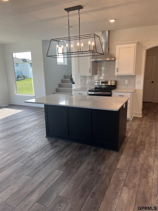 kitchen featuring wall chimney range hood, hanging light fixtures, electric stove, dark hardwood / wood-style floors, and white cabinetry