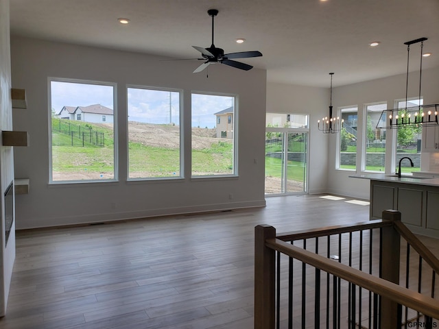 unfurnished living room featuring sink, light hardwood / wood-style floors, and ceiling fan with notable chandelier