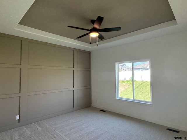 unfurnished bedroom featuring ceiling fan, light colored carpet, and a raised ceiling