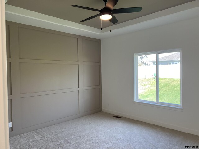 unfurnished bedroom with ceiling fan, a tray ceiling, and light carpet