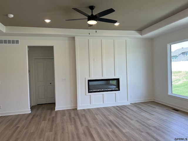 unfurnished living room with ceiling fan, light wood-type flooring, and a tray ceiling