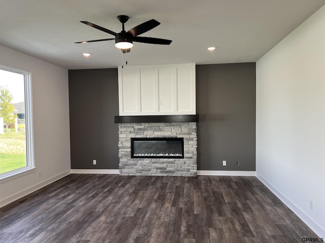 unfurnished living room featuring dark hardwood / wood-style floors, a stone fireplace, a wealth of natural light, and ceiling fan