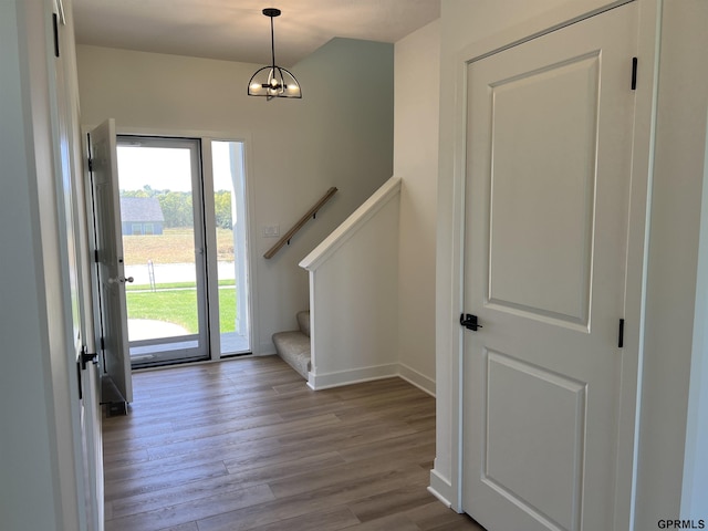 foyer entrance featuring stairway, wood finished floors, baseboards, and a chandelier