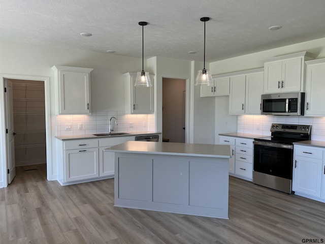 kitchen with pendant lighting, sink, light wood-type flooring, white cabinetry, and stainless steel appliances