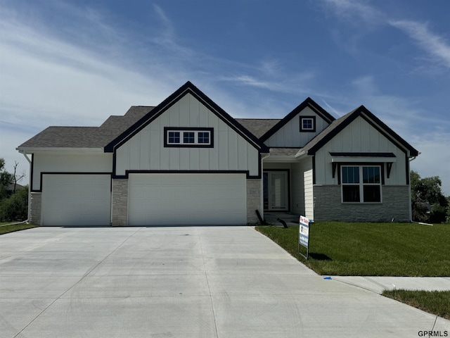 view of front of property featuring roof with shingles, concrete driveway, board and batten siding, a front yard, and stone siding