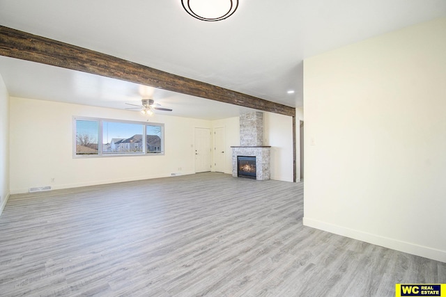 unfurnished living room with ceiling fan, a fireplace, beamed ceiling, and light hardwood / wood-style floors