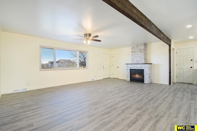 unfurnished living room with a stone fireplace, ceiling fan, beamed ceiling, and light wood-type flooring