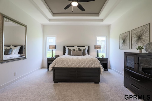 bedroom featuring multiple windows, light colored carpet, and a tray ceiling