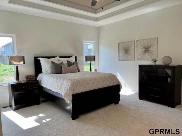 carpeted bedroom featuring multiple windows, ceiling fan, and a tray ceiling