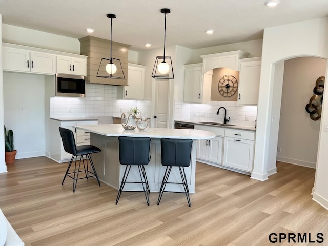 kitchen with sink, white cabinetry, stainless steel microwave, a kitchen island, and pendant lighting