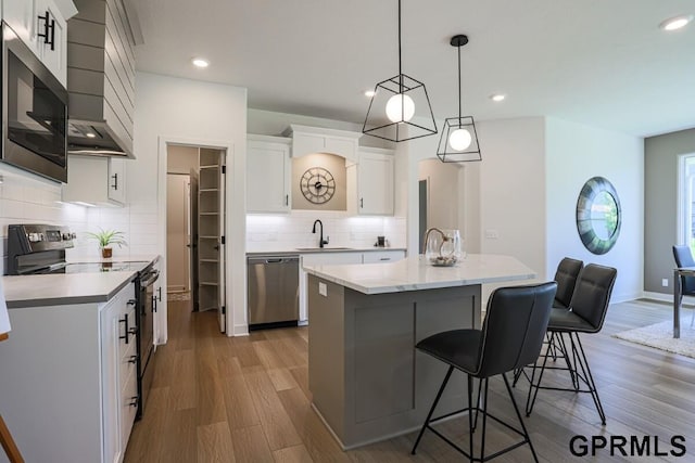 kitchen featuring appliances with stainless steel finishes, an island with sink, sink, white cabinets, and hanging light fixtures