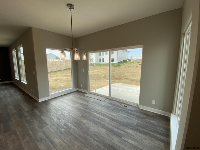 unfurnished dining area featuring a healthy amount of sunlight, dark hardwood / wood-style flooring, and a notable chandelier