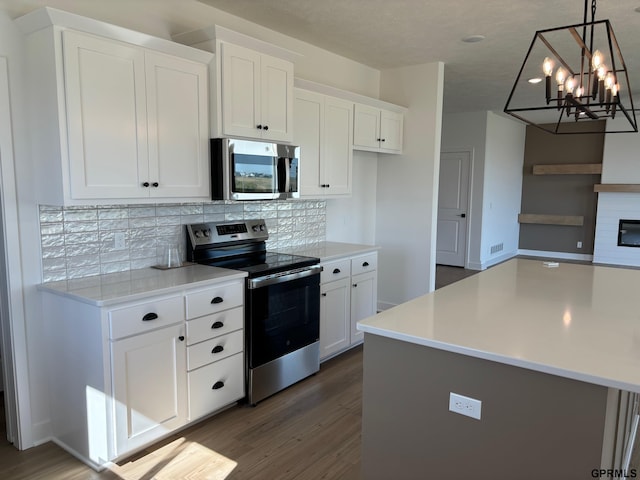 kitchen featuring dark wood-type flooring, tasteful backsplash, decorative light fixtures, white cabinets, and appliances with stainless steel finishes