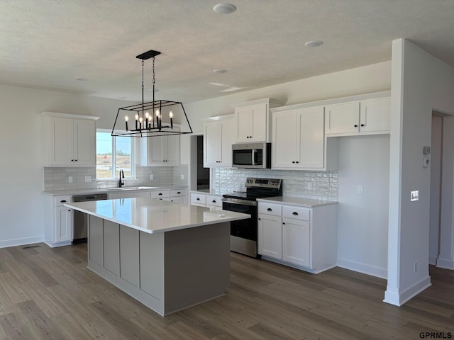 kitchen with a center island, sink, hardwood / wood-style flooring, appliances with stainless steel finishes, and white cabinetry