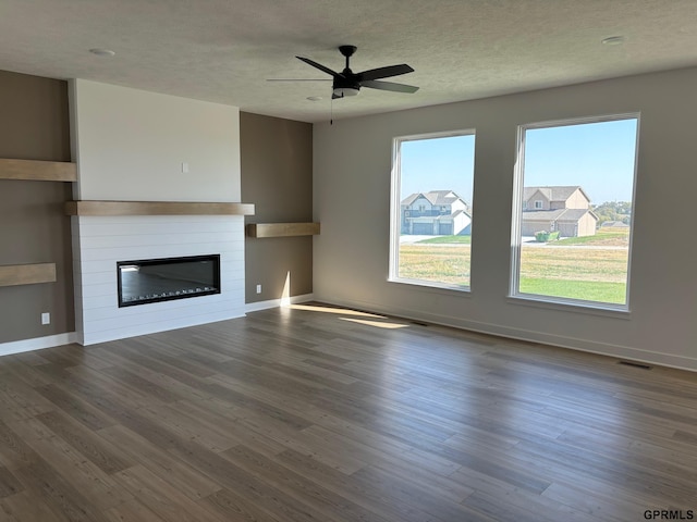 unfurnished living room featuring a fireplace, a textured ceiling, dark hardwood / wood-style flooring, and ceiling fan