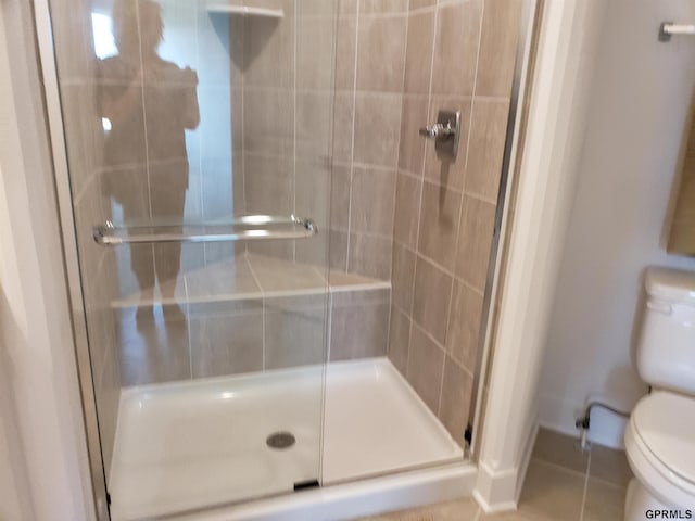 bathroom featuring tile patterned flooring, toilet, and a shower with shower door