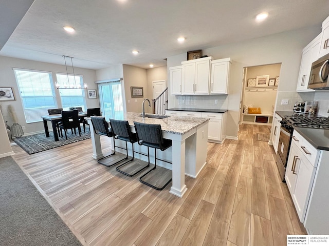 kitchen featuring a kitchen island with sink, white cabinets, hanging light fixtures, sink, and appliances with stainless steel finishes