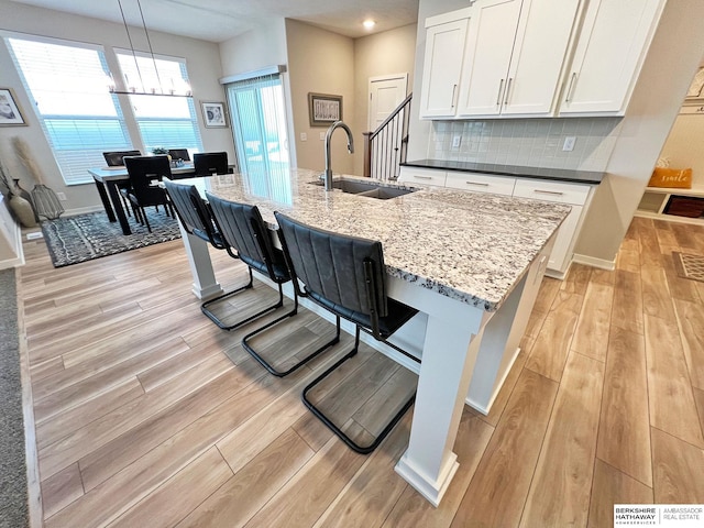 kitchen with a kitchen island with sink, sink, pendant lighting, light hardwood / wood-style floors, and white cabinetry