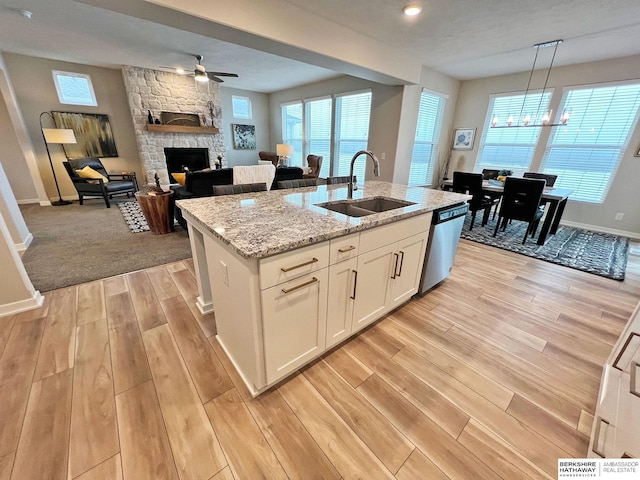 kitchen with white cabinetry, sink, hanging light fixtures, stainless steel dishwasher, and a center island with sink