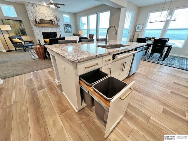 kitchen with sink, white cabinetry, hanging light fixtures, a stone fireplace, and an island with sink